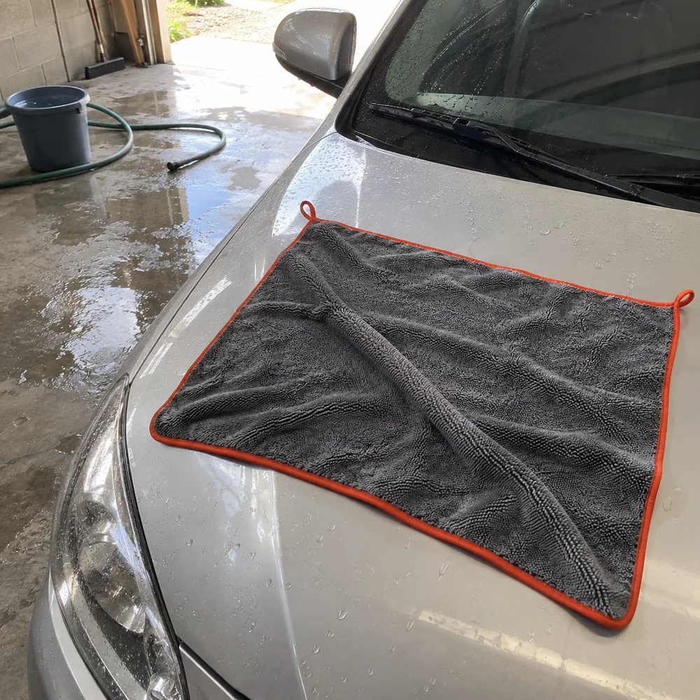 Cena ilustrativa da toalha cinza com borda laranja sobre o capô molhado na garagem